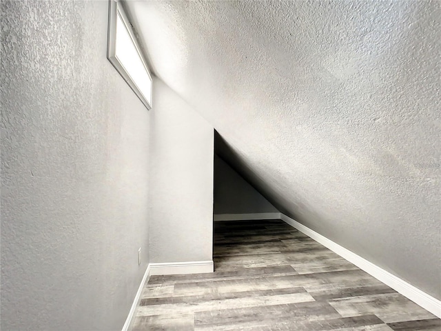 stairway with wood-type flooring, vaulted ceiling, and a textured ceiling