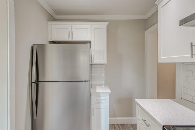 kitchen with stainless steel refrigerator, white cabinetry, ventilation hood, backsplash, and ornamental molding