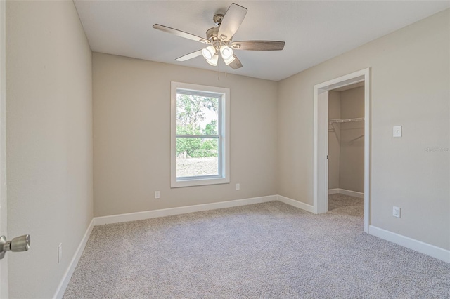 unfurnished bedroom with a spacious closet, a closet, ceiling fan, and light colored carpet