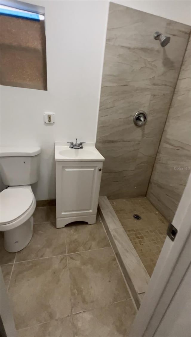 bathroom featuring a tile shower, vanity, toilet, and tile patterned floors