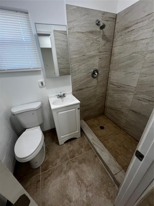 bathroom featuring tile patterned floors, toilet, a tile shower, and vanity