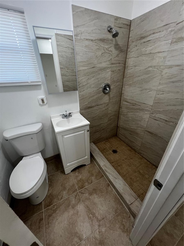 bathroom featuring a tile shower, tile patterned flooring, vanity, and toilet