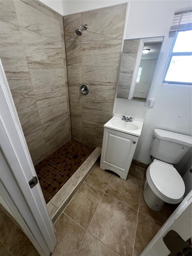 bathroom with tile patterned flooring, toilet, a tile shower, and vanity