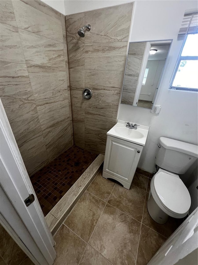 bathroom with tile patterned flooring, toilet, a tile shower, and vanity