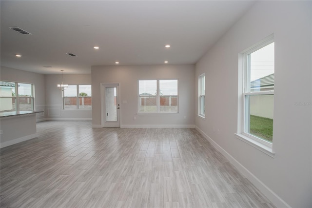 unfurnished living room with light wood-type flooring and a chandelier