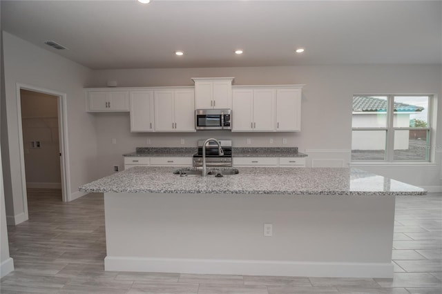 kitchen featuring an island with sink, sink, white cabinetry, and appliances with stainless steel finishes