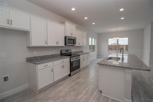 kitchen featuring a center island with sink, white cabinetry, light stone countertops, appliances with stainless steel finishes, and sink