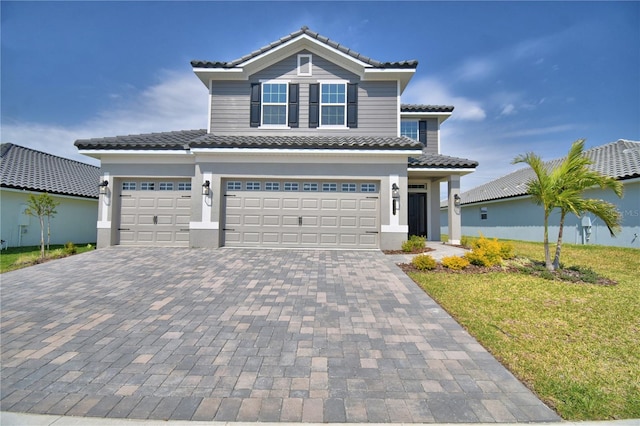 view of front of house featuring decorative driveway, a garage, a tile roof, a front lawn, and stucco siding