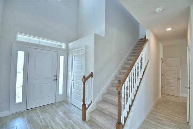 foyer with baseboards, stairs, a towering ceiling, and light wood-type flooring