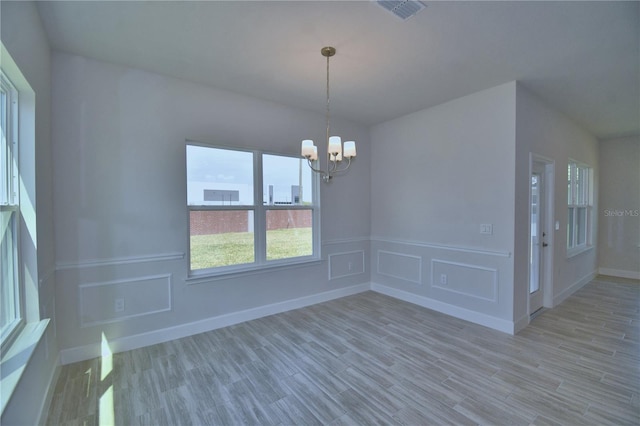 unfurnished dining area with a decorative wall, visible vents, a chandelier, and wood finished floors