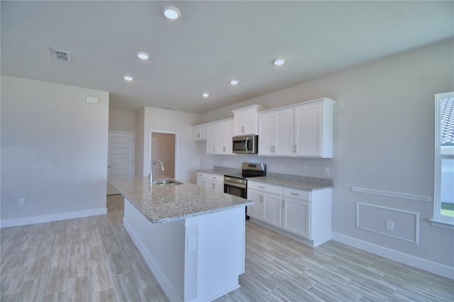 kitchen with a sink, white cabinetry, a center island with sink, light wood-type flooring, and stainless steel appliances
