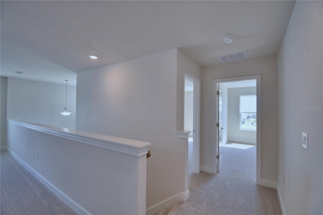 hallway with baseboards, an upstairs landing, visible vents, and light carpet