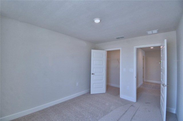 unfurnished bedroom with a closet, visible vents, baseboards, light carpet, and a spacious closet
