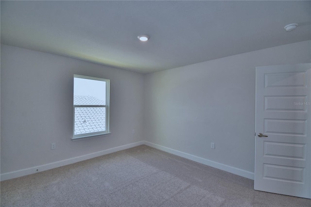 spare room featuring light colored carpet and baseboards