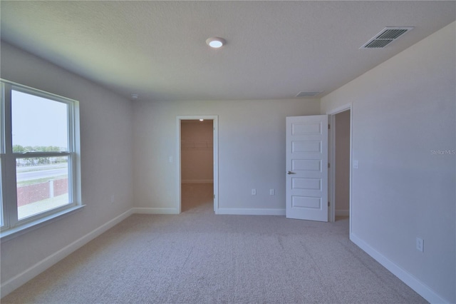 spare room featuring baseboards, visible vents, light colored carpet, and a textured ceiling