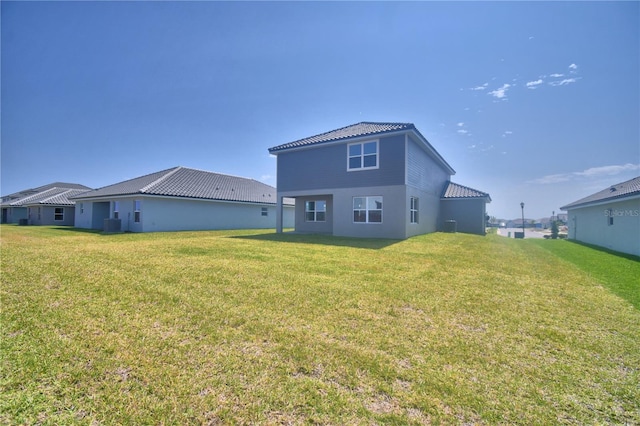 back of house featuring a lawn, central AC unit, a tiled roof, and stucco siding
