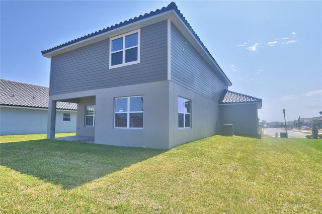 back of house featuring a tiled roof, central AC unit, stucco siding, and a lawn