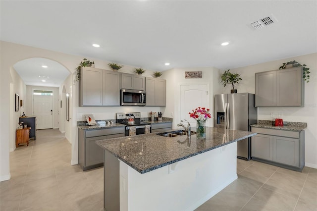 kitchen with appliances with stainless steel finishes, arched walkways, a sink, and gray cabinetry