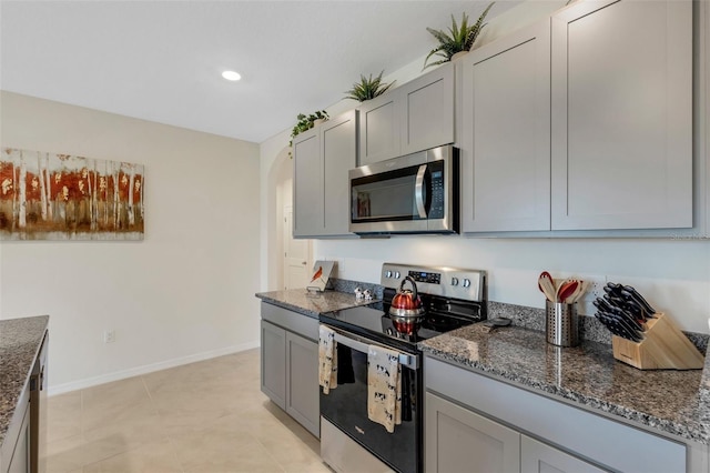 kitchen featuring baseboards, arched walkways, appliances with stainless steel finishes, dark stone countertops, and gray cabinets