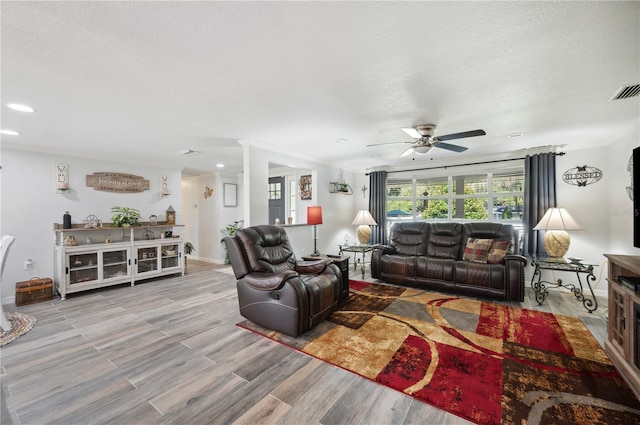 living room featuring wood-type flooring, a textured ceiling, ceiling fan, and ornamental molding