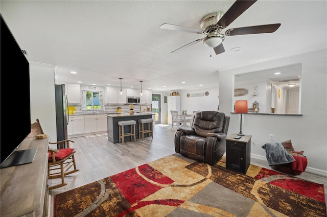 living room with light hardwood / wood-style floors, ceiling fan, and crown molding