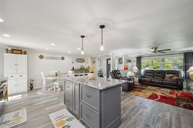 kitchen featuring hanging light fixtures, ceiling fan, a kitchen island, light stone counters, and white cabinetry