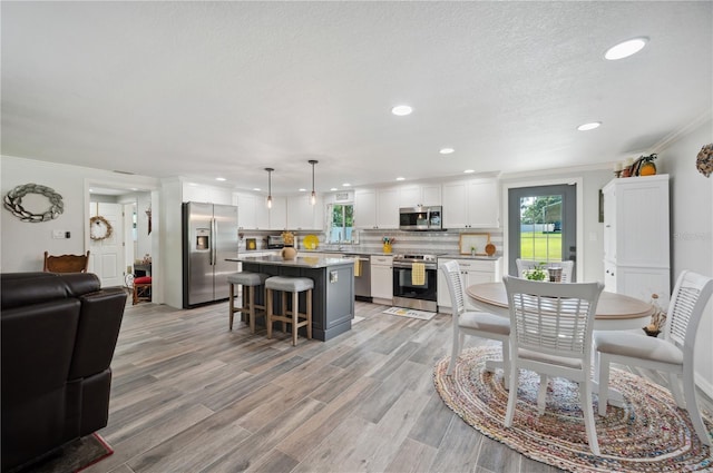 kitchen with white cabinetry, a center island, hanging light fixtures, stainless steel appliances, and a kitchen breakfast bar