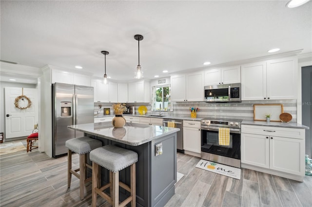 kitchen featuring stainless steel appliances, pendant lighting, white cabinets, a center island, and a breakfast bar area