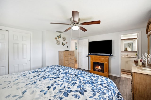 bedroom featuring dark hardwood / wood-style flooring, a closet, ensuite bath, and ceiling fan