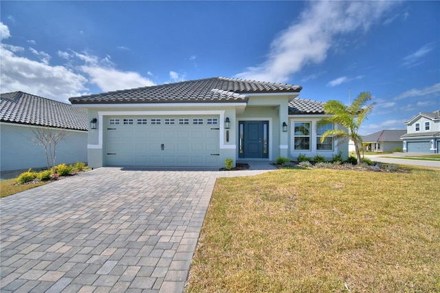 view of front of home with a garage, a tiled roof, decorative driveway, a front lawn, and stucco siding