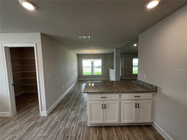 kitchen with white cabinets, hardwood / wood-style flooring, dark stone counters, and an inviting chandelier