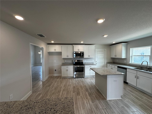 kitchen with appliances with stainless steel finishes, light wood-type flooring, sink, a center island, and white cabinetry