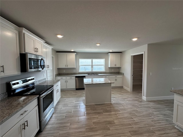 kitchen with light stone countertops, stainless steel appliances, a kitchen island, sink, and white cabinetry