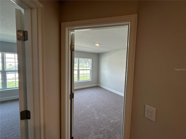 hall featuring carpet flooring and a textured ceiling