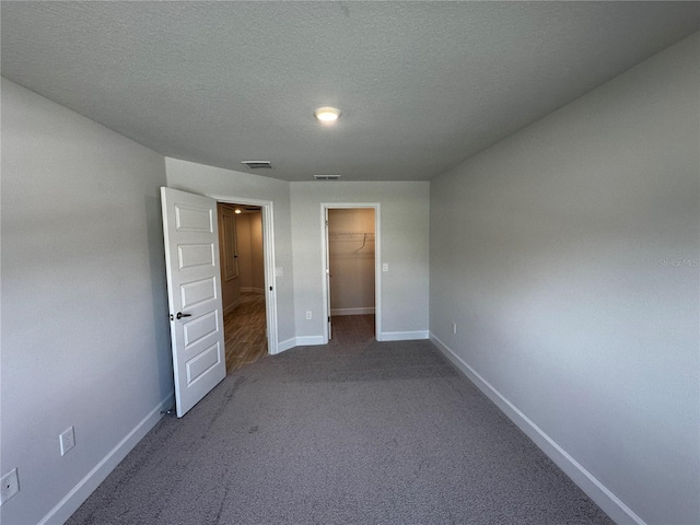 unfurnished bedroom featuring a textured ceiling, carpet floors, a spacious closet, and a closet