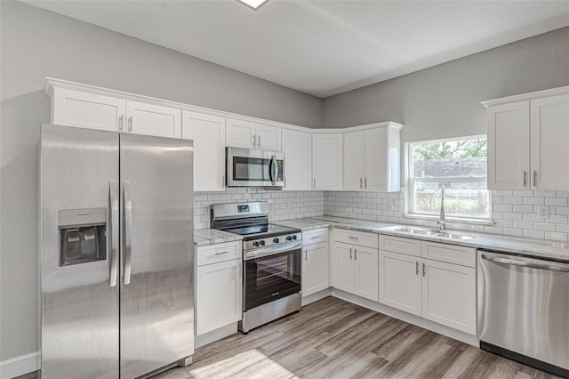 kitchen featuring backsplash, sink, light stone countertops, white cabinetry, and stainless steel appliances