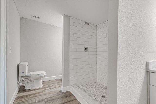 bathroom featuring hardwood / wood-style floors, vanity, toilet, and tiled shower