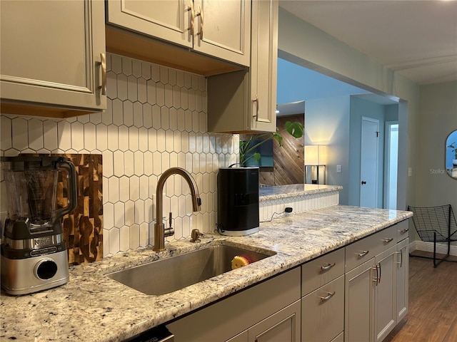 kitchen featuring light stone countertops, wood-type flooring, backsplash, and sink