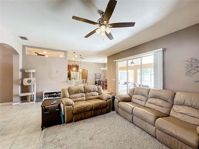 living room featuring ceiling fan with notable chandelier, light tile patterned floors, and a textured ceiling