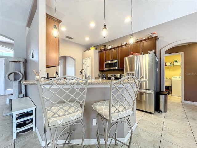 kitchen featuring kitchen peninsula, a kitchen breakfast bar, stainless steel appliances, decorative light fixtures, and light tile patterned flooring