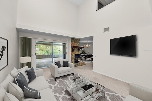 living room featuring a towering ceiling, light colored carpet, a stone fireplace, and a notable chandelier