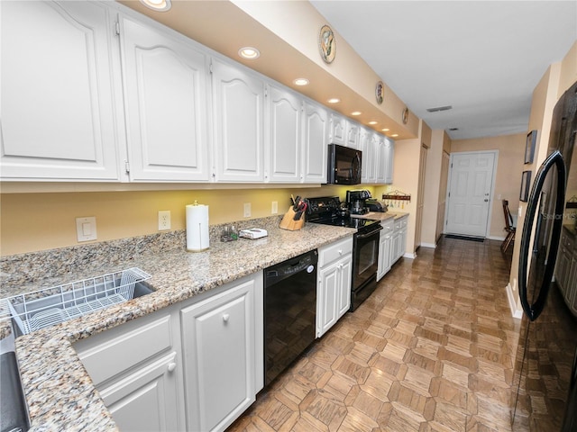 kitchen with light parquet floors, light stone counters, white cabinetry, and black appliances