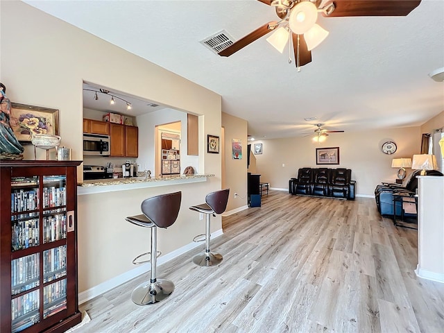 kitchen with a kitchen bar, light hardwood / wood-style flooring, light stone counters, kitchen peninsula, and stainless steel appliances