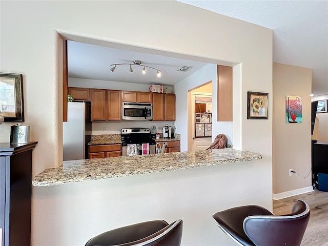 kitchen featuring kitchen peninsula, appliances with stainless steel finishes, light stone counters, and a breakfast bar area