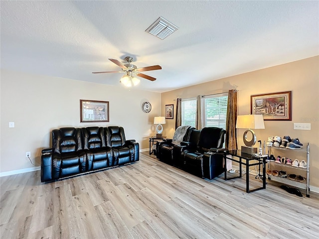 living room featuring ceiling fan, light wood-type flooring, and a textured ceiling