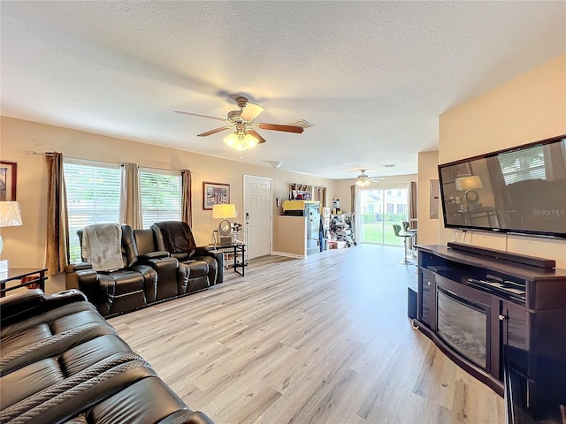 living room featuring ceiling fan, a healthy amount of sunlight, light hardwood / wood-style floors, and a textured ceiling