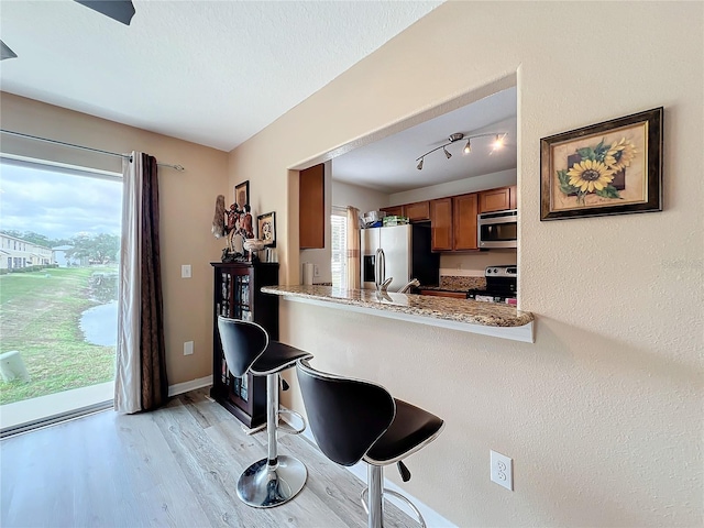 kitchen with appliances with stainless steel finishes, light hardwood / wood-style floors, light stone counters, and plenty of natural light