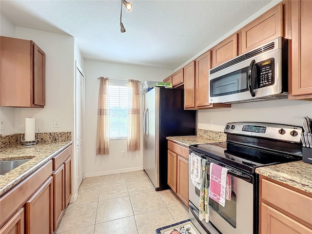 kitchen with light stone countertops, a textured ceiling, stainless steel appliances, sink, and light tile patterned floors