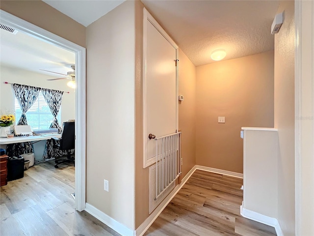 corridor featuring light wood-type flooring and a textured ceiling