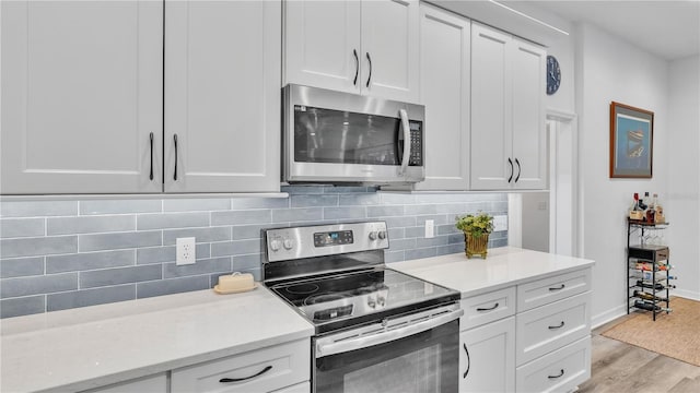 kitchen with white cabinets, decorative backsplash, light hardwood / wood-style floors, light stone counters, and stainless steel appliances